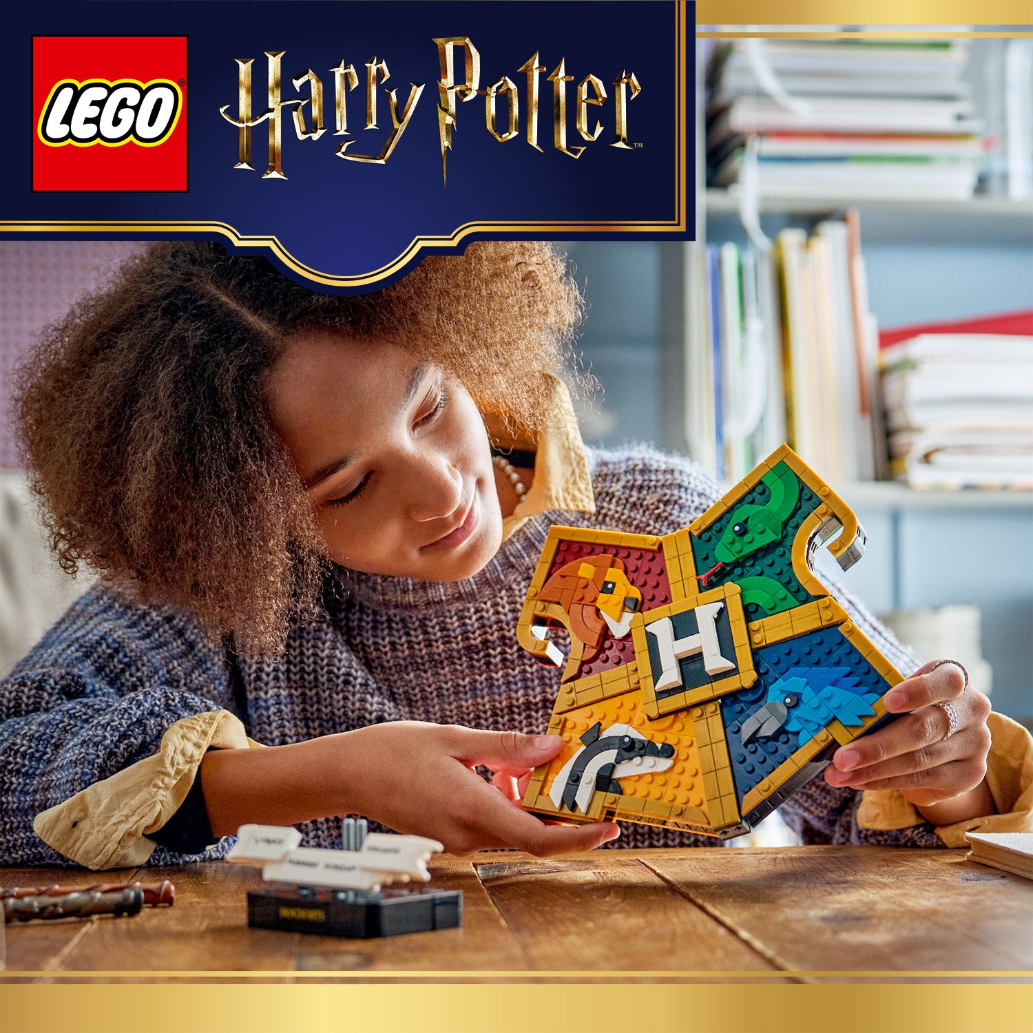 Junge Frau hält ein LEGO Modell des Hogwarts-Hauswappens aus Harry Potter in den Händen und betrachtet es an einem Holztisch