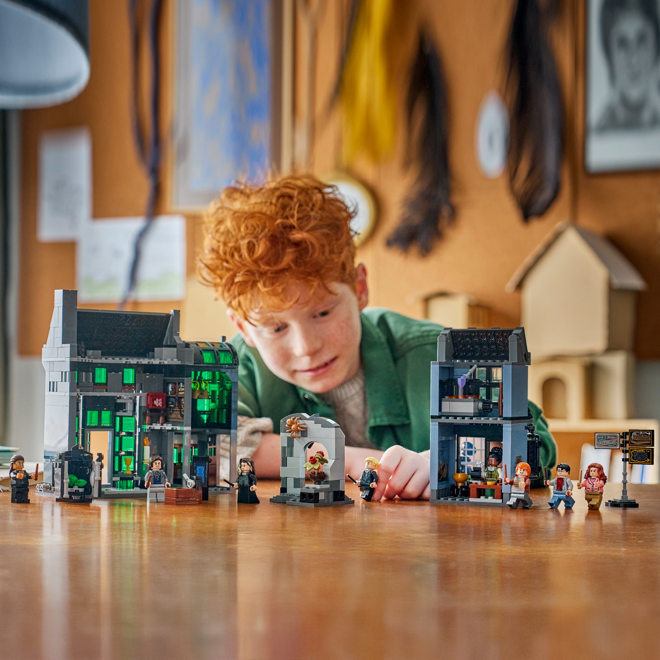 Kind mit roten Haaren spielt mit LEGO Zaubererladen-Sets und Minifiguren auf einem Holztisch