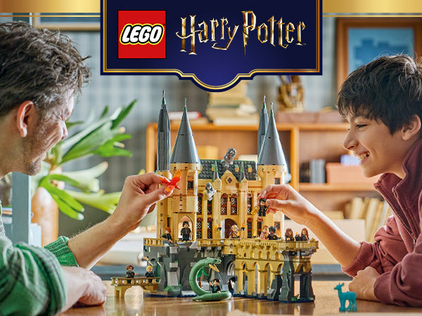 Zwei Personen spielen mit einem LEGO Harry Potter Schloss Hogwarts Ostflügel mit mehreren Türmen und Minifiguren auf einem Tisch in einem Wohnzimmer.