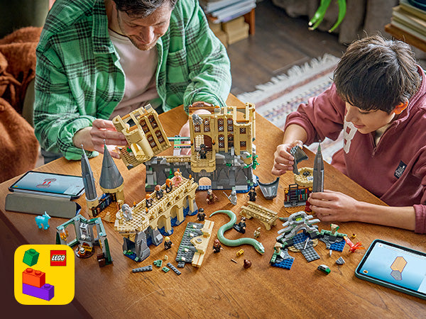 Zwei Kinder bauen am Tisch ein LEGO Set des Hogwarts-Ostflügels mit mehreren Gebäudeteilen, Minifiguren und Zubehör.