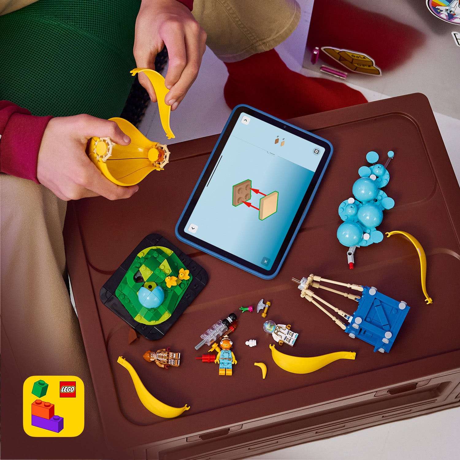 Kind baut mit LEGO Figuren und -Teilen auf einem Tisch, daneben ein Tablet mit Bauanleitung und mehrere gelbe LEGO Teile.