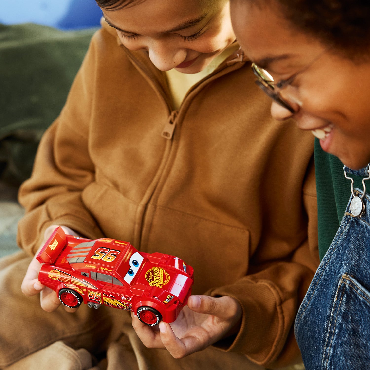 Kind hält ein rotes LEGO Modellauto von Lightning McQueen aus der Speed Champion Serie, erkennbar an der Nummer 95 und den Augen auf der Windschutzscheibe.