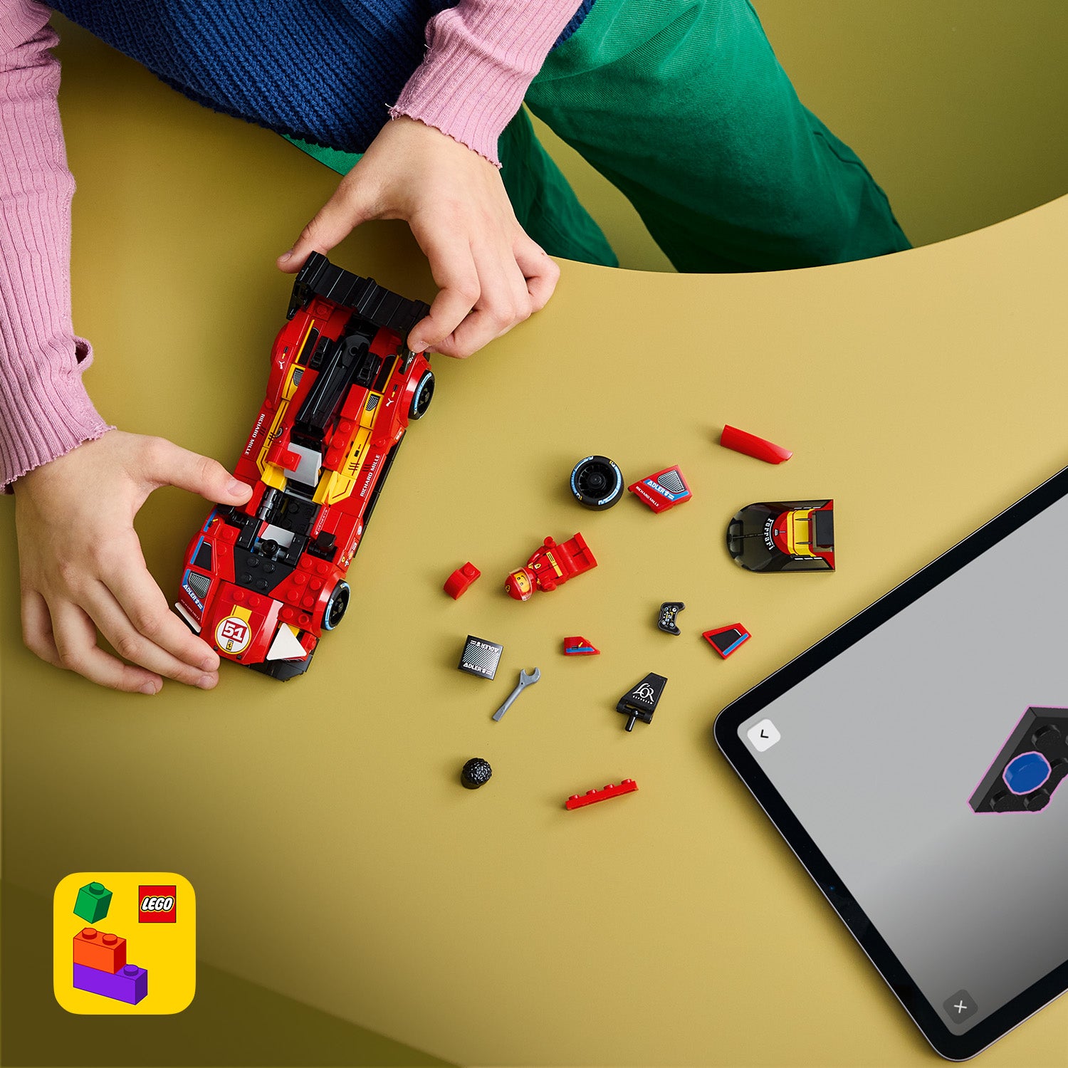Hände halten ein rotes LEGO Ferrari-Modellauto neben verstreuten LEGO Teilen und einem Tablet mit Bauanleitung auf einem gelben Tisch