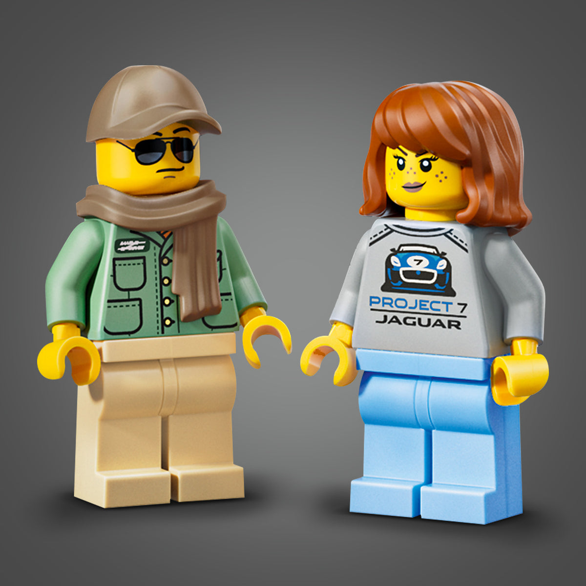 Zwei LEGO Minifiguren, eine mit brauner Mütze, Sonnenbrille, grünem Jackett und beiger Hose, die andere mit roten Haaren, grauem Pullover mit 'PROJECT 7 JAGUAR'-Aufdruck und blauer Hose