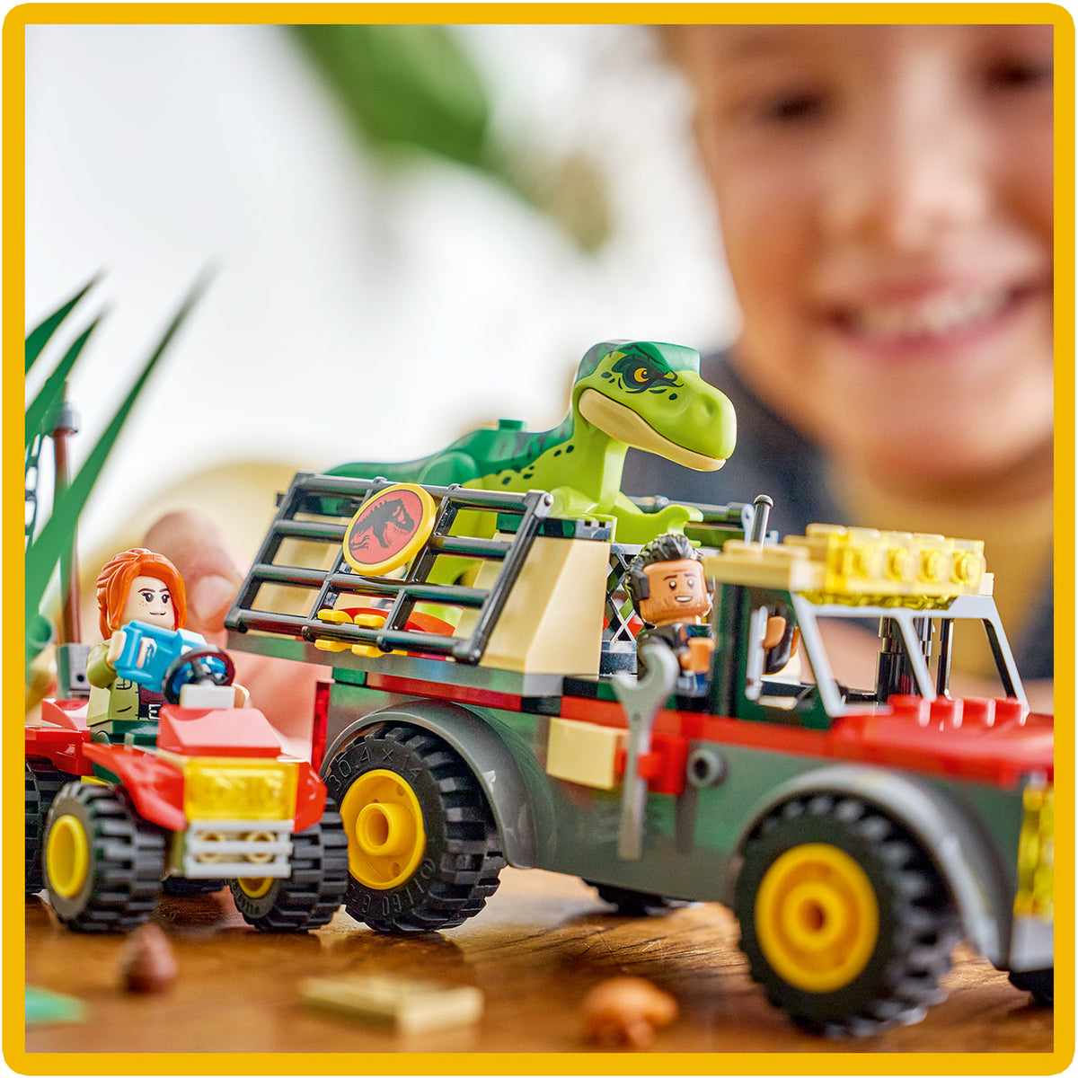 Spielszene mit LEGO Transporter und Dinosaurierfigur, zwei LEGO Figuren sitzen auf Fahrzeugen, im Hintergrund unscharf ein lächelndes Kind